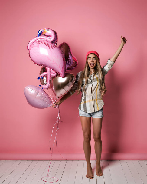 ピンクのパステルの背景にピンクの風船の束を保持している美しい若い喜びの女の子. - 写真・画像