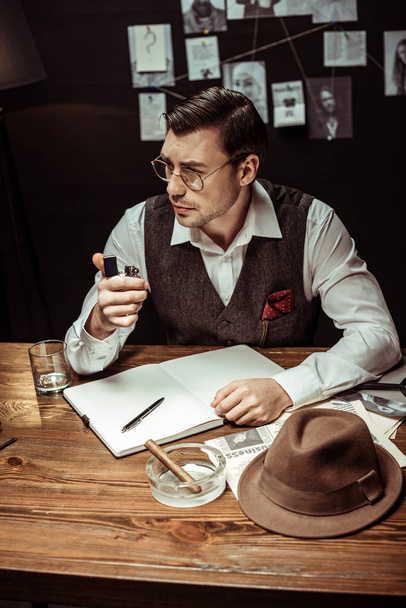 Швидкий детектив в окулярах сидить за столом і тримає запальничку в офісі
 - Фото, зображення