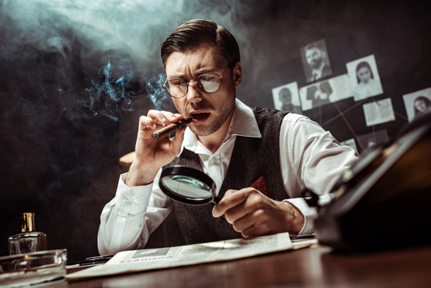 Detective in glasses smoking cigar and reading newspaper with magnifier in office - Foto, immagini