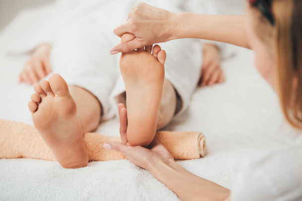 vista parcial de masajista haciendo masaje de pies a mujer adulta en spa
 - Foto, Imagen
