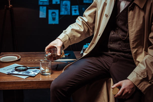 Osittainen näkymä etsivä kaatamalla konjakkia lasiin istuessaan pöydällä
 - Valokuva, kuva