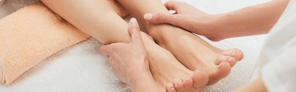 panoramic shot of masseur doing foot massage to adult woman in spa - Photo, image