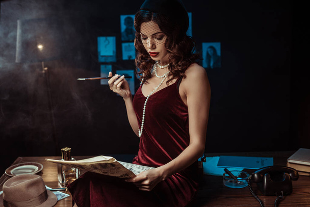 Kobieta z ustnik siedzi na stole i czytania gazety w ciemnym biurze - Zdjęcie, obraz