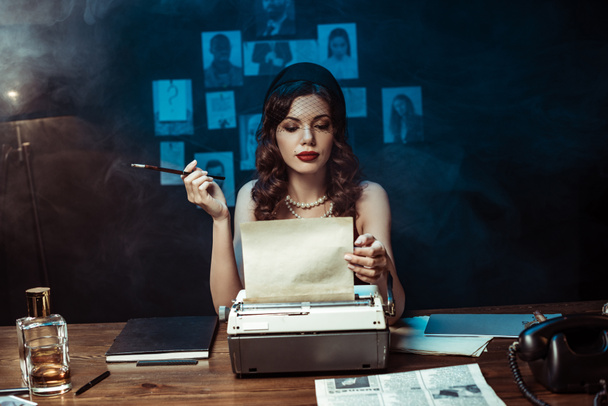 Mujer pensativa con boquilla usando máquina de escribir en oficina oscura
 - Foto, imagen