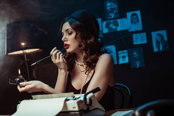 Beautiful woman with mouthpiece lighting cigarette with lighter in dark office - Foto, Imagem