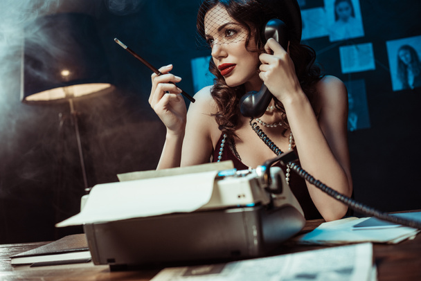 Mujer atractiva con la boquilla hablando por teléfono en la oficina oscura
 - Foto, imagen