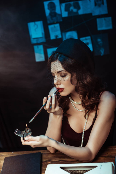Beautiful woman with mouthpiece lighting cigarette with lighter in dark office - Foto, afbeelding