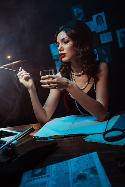 Belle femme au chapeau fascinant tenant embout buccal et verre de cognac dans un bureau sombre
 - Photo, image