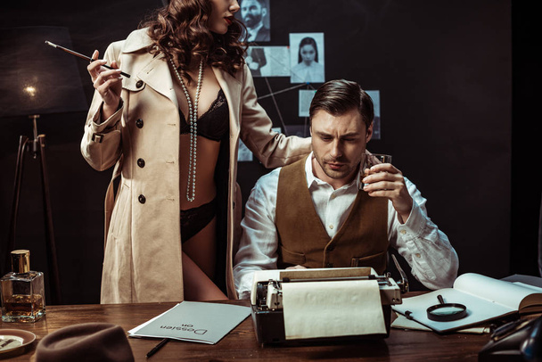 Cropped view of sexy woman in underwear and trench coat seducing detective with glass of cognac - Photo, Image