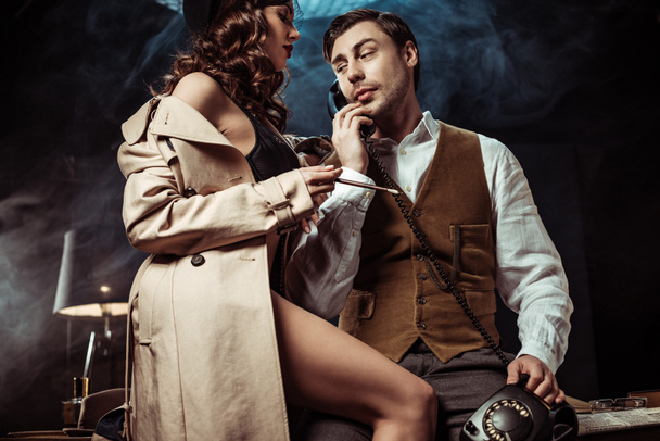 Low angle view of sexy woman in underwear and trench coat seducing detective in office - Fotografie, Obrázek