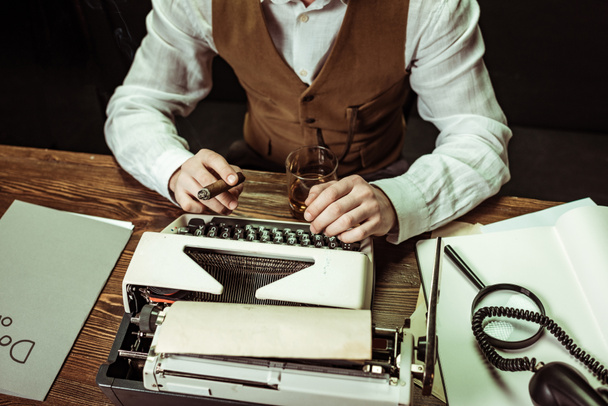 Vista parcial del detective con cigarro usando máquina de escribir en la oficina
 - Foto, Imagen