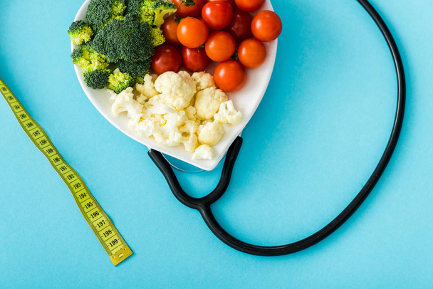 organická zelenina na desce v blízkosti měřicí pásky a stetoskop na modrém - Fotografie, Obrázek