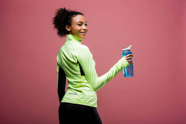 beautiful smiling african american sportswoman in track jacket with sport bottle looking at camera isolated on brown - Foto, afbeelding
