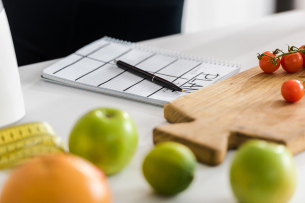 selective focus of wooden cutting board with cherry tomatoes near notebook with plan lettering - Fotografie, Obrázek