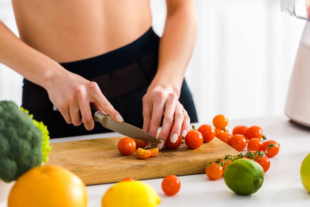 cropped view of woman cutting cherry tomatoes on wooden cutting board  - Foto, Bild