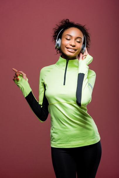 beautiful african american sportswoman in headphones listening music with eyes closed isolated on brown - Fotoğraf, Görsel