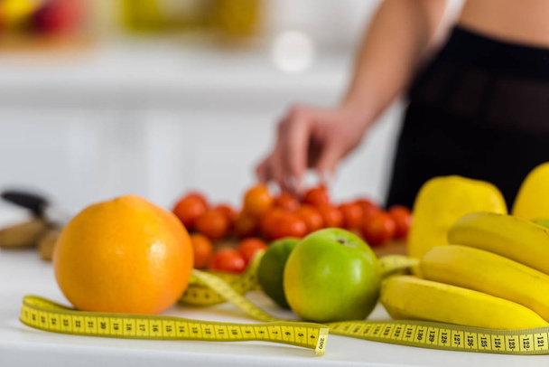 cropped view of woman taking cherry tomato near measuring tape in kitchen  - Foto, immagini