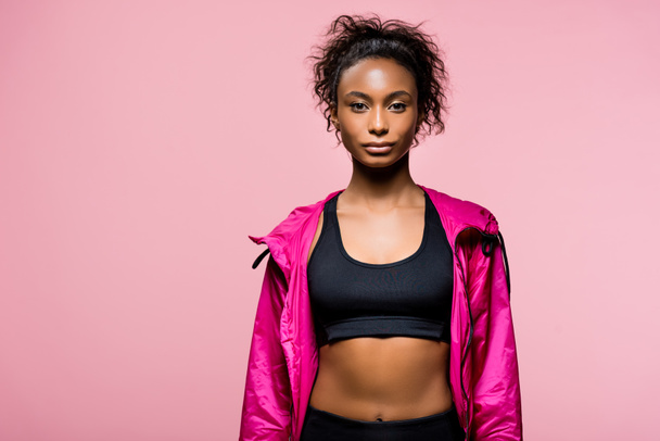 confident attractive african american sportswoman in windbreaker looking at camera isolated on pink with copy space - Фото, зображення