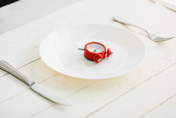 white plate with cutlery near red alarm clock on wooden surface  - Φωτογραφία, εικόνα