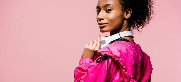 panoramic shot of beautiful african american sportswoman with headphones looking at camera isolated on pink - Foto, immagini
