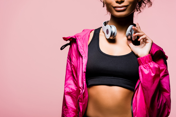 Ausgeschnittene Ansicht einer afrikanisch-amerikanischen Sportlerin mit Kopfhörern isoliert auf rosa mit Kopierraum - Foto, Bild