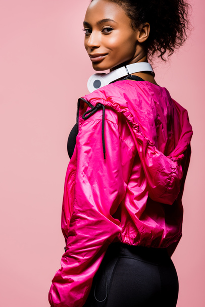 beautiful african american sportswoman with headphones looking at camera isolated on pink - 写真・画像