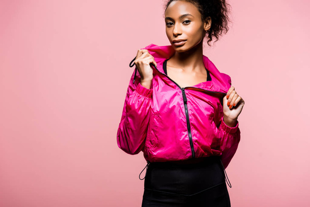 attractive african american sportswoman in windbreaker looking at camera isolated on pink with copy space - Foto, Bild