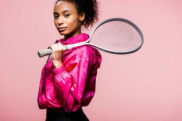 beautiful african american sportswoman looking at camera while posing with tennis racket isolated on pink - Foto, Imagen