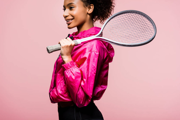 kaunis hymyilevä afrikkalainen amerikkalainen urheilija tilalla tennismaila eristetty vaaleanpunainen
 - Valokuva, kuva