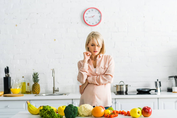 pensive blonde pregnant woman looking at fruits and vegetables  - Foto, Imagen