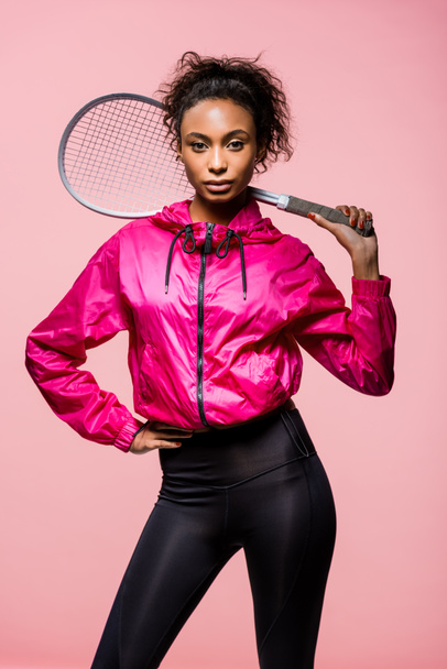 bela esportista afro-americana segurando raquete de tênis e olhando para a câmera isolada em rosa
 - Foto, Imagem
