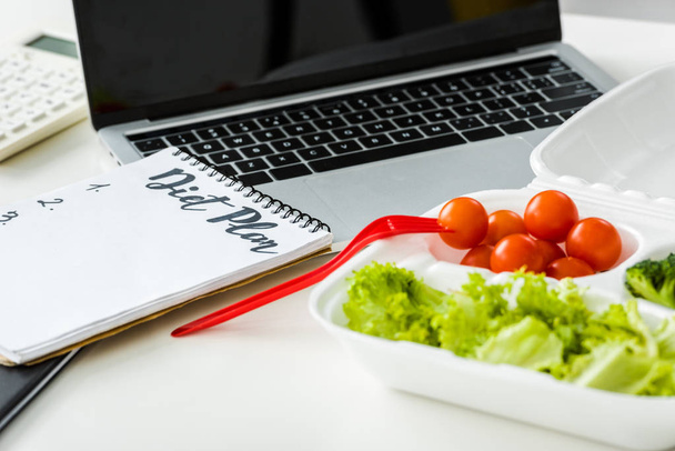 Leckeres Gemüse in der Nähe von Notizbuch mit Ernährungsplan-Schriftzug und Laptop - Foto, Bild