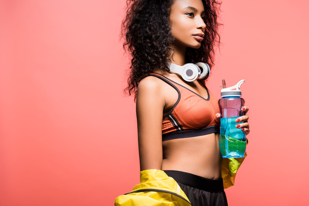 beautiful african american sportswoman posing with headphones and sport bottle isolated on coral with copy space - Foto, Bild