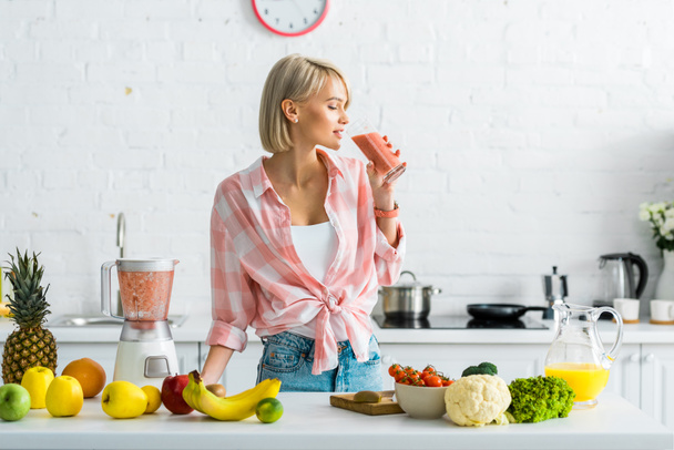 attraente donna bionda bere gustoso frullato vicino ingredienti in cucina
  - Foto, immagini