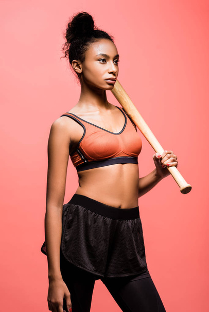 bella sportiva africana americana in posa con mazza da baseball isolata sul corallo
  - Foto, immagini
