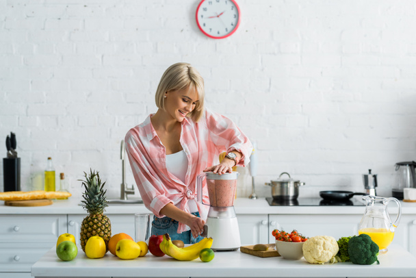 happy young woman preparing tasty nutritious smoothie in blender  - Photo, Image