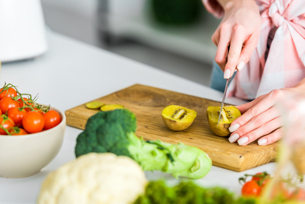 cropped view of girl cutting kiwi fruit near ingredients in kitchen - 写真・画像