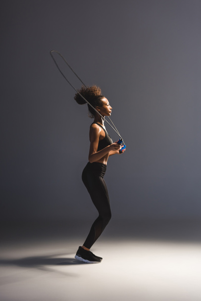 athletic african american sportswoman exercising with skipping rope on grey - Foto, Imagem