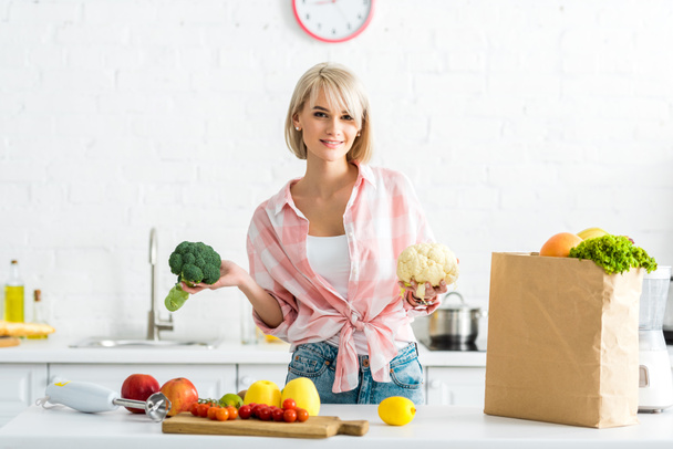 iloinen blondi tyttö tilalla kukkakaali ja parsakaali keittiössä
  - Valokuva, kuva