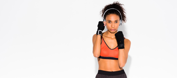 panoramic shot of athletic african american sportswoman in sport gloves looking at camera on white - Photo, Image