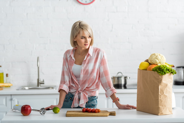 Blondine steht Papiertüte mit Lebensmitteln in Küche  - Foto, Bild