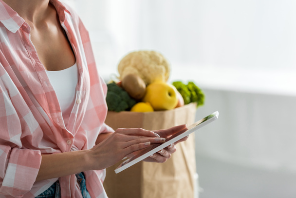 cropped view of woman using digital tablet near paper bag with ingredients   - Fotoğraf, Görsel