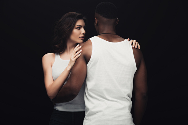 beautiful seductive woman embracing african american man isolated on black - Photo, Image