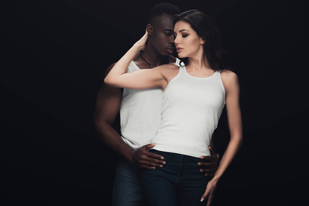 passionate african american man embracing beautiful woman isolated on black - Фото, изображение
