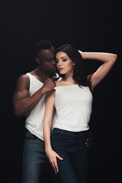 handsome african american man undressing beautiful sensual woman isolated on black - Photo, Image