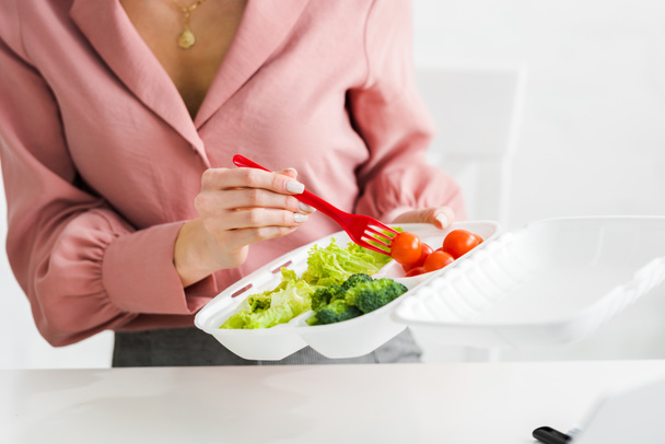 cropped view of  woman holding takeaway box with organic vegetables and plastic fork  - 写真・画像