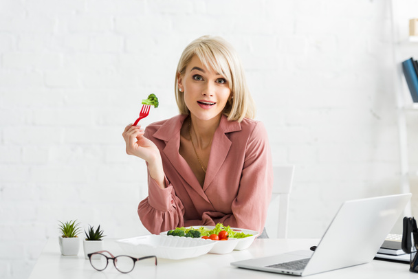 surprise blonde pigiste tenant fourchette avec tomate cerise près d'un ordinateur portable
 - Photo, image