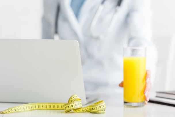 cropped view of nutritionist holding glass of fresh orange juice near measuring tape  - Photo, Image
