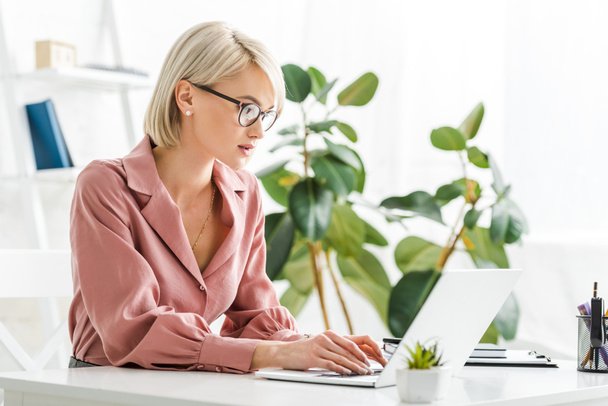 attractive young blonde freelancer in glasses typing on laptop  - Foto, Bild