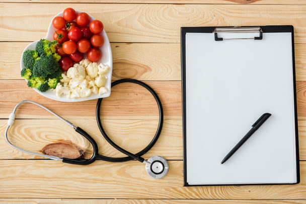 top view of blank clipboard with pen near stethoscope and tasty vegetables on heart-shape plate - Zdjęcie, obraz
